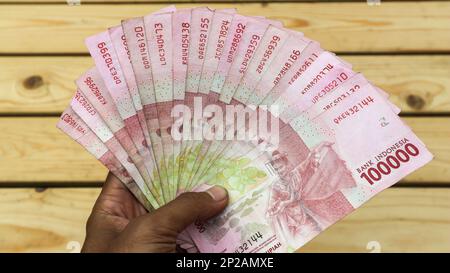hand holding IDR 100,000 rupiah note isolated on white background ...