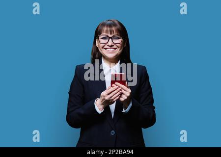 Smiling middle aged business woman using smartphone, blue background Stock Photo