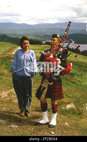 1970s, historical, a young woman standing for a photo beside a scottish piper in full Highland Dress playing his bagpipes, Braemar, Scotland, UK. Stock Photo