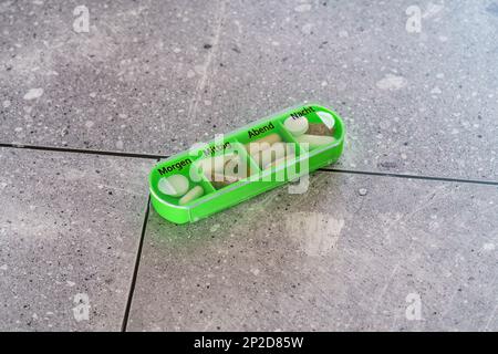 Coloured pill box with four slots, one slot open. Box for one day, german letters Stock Photo