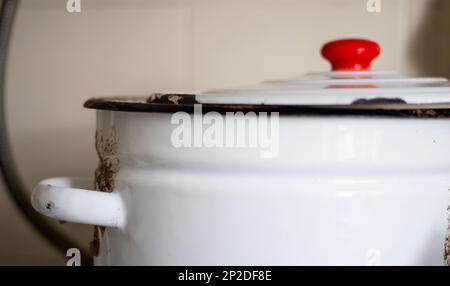 One large white pot with a lid and a red handle sits on a tile in a restaurant or home kitchen. Stock Photo