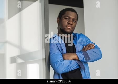 Close-up black serious male face in profile. Man stand with arms folded. Portrait of pensive african american man looking out window in office Stock Photo
