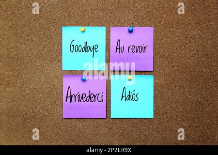 Multicolor notes with important message, motivation and reminders on cork board 'Goodbye' in different languages: English, French, Spanish, Italian Stock Photo