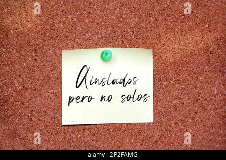 White note on cork board with message in Spanish language 'Isolated but not alone' Stock Photo