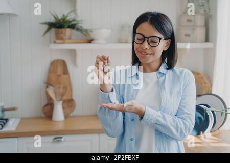 Happy female homeowner or tenant showing keys to new home, standing in kitchen. Woman holding key of house or apartment, satisfied with housing purcha Stock Photo
