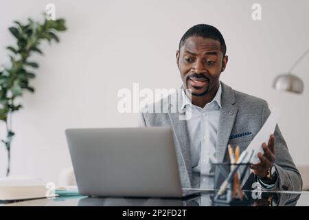 Perplexed african american male worker looking at laptop screen received dismissal notice. Puzzled black guy businessman reading bad news in email or Stock Photo