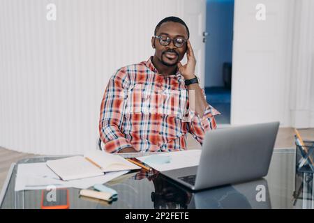 Tired african american male worker with closed eyes hold head with hand relax, have a break at workplace. Pensive black man at laptop collect thoughts Stock Photo