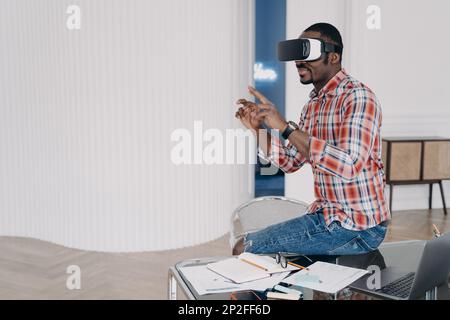 Businessman has virtual course. African american man in vr glasses at home. Virtual reality headset using, electronic device. Modern education and dig Stock Photo