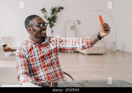 Happy afro man has video call on phone and talks to friend. Businessman stays home on quarantine and working remotely. Consulting or corporate meeting Stock Photo
