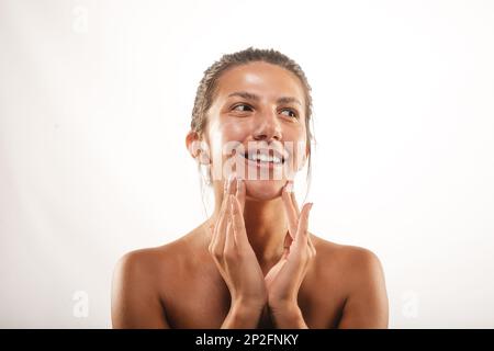 Close up of a beautiful girl smearing a face cream while smiling at the studio on a white backround Stock Photo