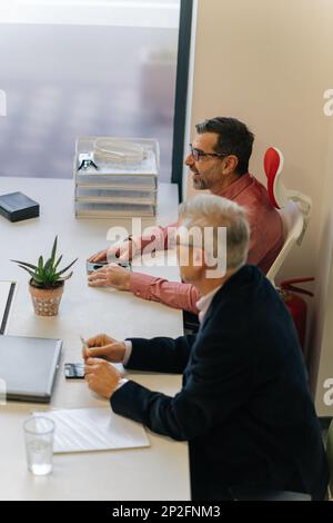 Two senior businesspeople sitting next to each other. They are talking to their younger colleagues Stock Photo