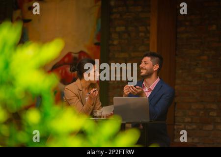 Two beautiful business colleagues are sitting in a cafe bar after work. They are having a fun gossip conversation Stock Photo