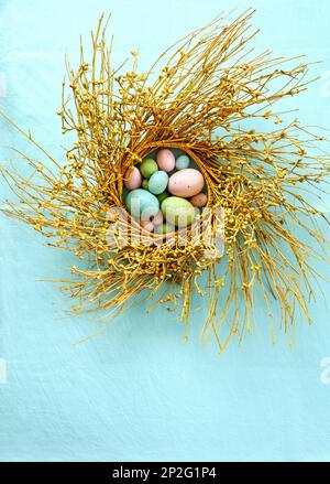 Pastel colored easter eggs in rustic berry branch wreath on turquoise background.  Vertical format shot from above in flat lay composition. Stock Photo
