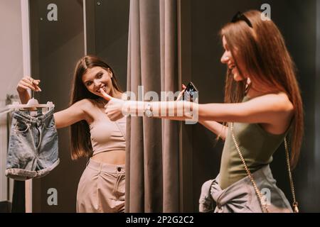 Two beauitful best friends standing in the changeing room. One of the showing the shorts the other one liking them Stock Photo