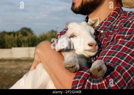 Farmer with cute goatling outdoors, closeup. Baby animal Stock Photo