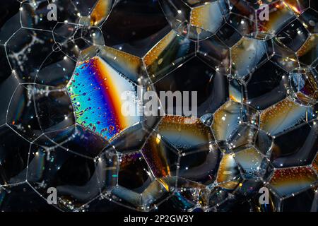 Close up, macro shot of a soap bubble, multicolored rainbow with yellow, purple, pink, blue and green colors on black background. Stock Photo