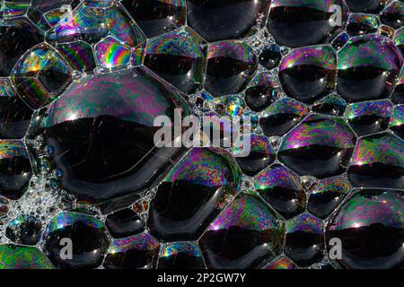 Close up, macro shot of a soap bubble, multicolored rainbow with yellow, purple, pink, blue and green colors on black background. Stock Photo