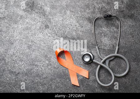 Orange ribbon and stethoscope on grey table, flat lay with space for text. Multiple sclerosis awareness Stock Photo