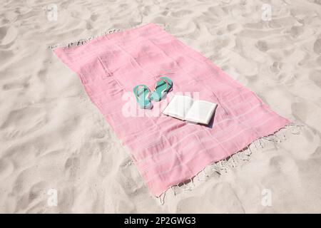 Pink striped beach towel, flip flops and book on sand Stock Photo