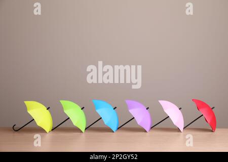 Small color umbrellas on wooden table against beige background. Space for text Stock Photo