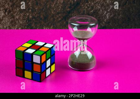 Plastic puzzle cube and hourglass on a pink table top Stock Photo