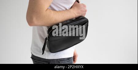 Side view man in a white t-shirt with a leather black handmade bag over his shoulder. Dark designer banana bag. Comfortable small bag for walking. Stock Photo