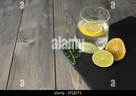 water with lemon homemade lemonade in a glass next to there are lemons with herb green rosemary on a black stand with a place for text. Healthy food d Stock Photo