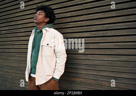 Cool young hipster gen z African American teen standing at wooden wall. Stock Photo