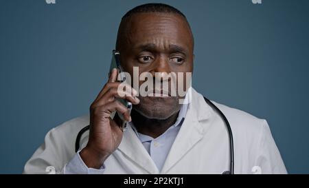 Portrait mature serious man talking on mobile phone focused puzzled confused professional doctor pediatrician therapist remotely communicates with Stock Photo