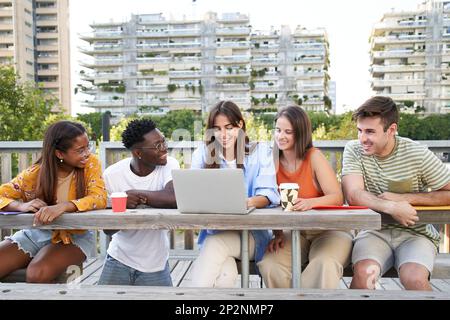 Group of cheerful multiracial students together happily looking at laptop outdoors. Portrait people. Stock Photo