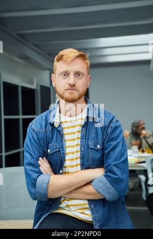 Vertical young red-haired programmer or businessman in modern office looking seriously at camera. Stock Photo