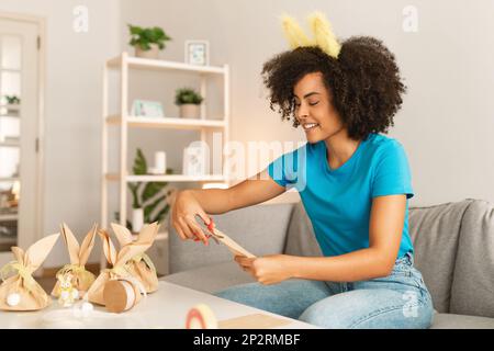 Easter Crafts. Black Woman Wearing Bunny Ears Making Gift Packaging At Home Stock Photo