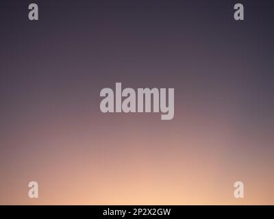 Sunset gradient in the sky. Abstract background with orange sunlight and a purple sky. The sky is clear and the colors are blending together. Stock Photo