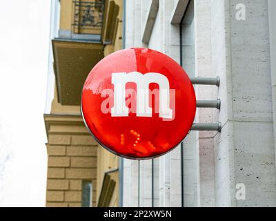 Red M dragee sign on a building facade. Advertisement for the m&m's store in Berlin. Chocolate brand of the Mars company. Popular US sweets. Stock Photo