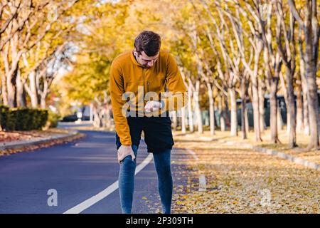 Man runner checking his pulse on the fitness tracker while exercising outdoors in autumn. Trees with yellow leaves on the background Stock Photo