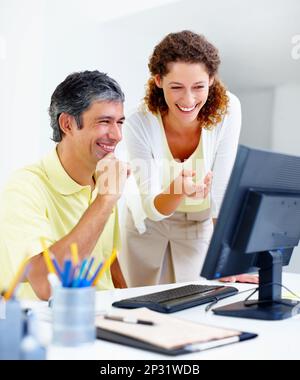 Executives working on computer. Male executive sitting at a table and working on computer with female colleague pointing at the screen. Stock Photo