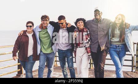 A group of multicultural friends walking together on the seaside promenade, arms around each other's shoulders - smiling and having a good time - the Stock Photo