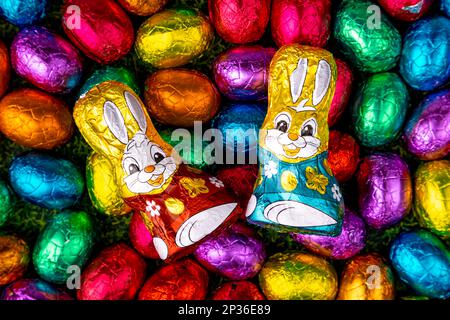 Colourful Easter sweets on grass, chocolate eggs and chocolate bunnies, full size Stock Photo