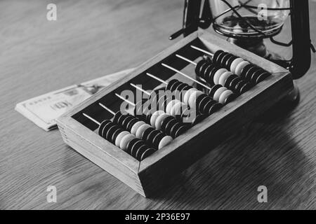 Old wooden abacus for counting money and dollars and an oil lamp nearby on a wooden table black and white photo Stock Photo