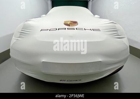 Perspective dynamic photo of sports car Porsche 911 Carrera in garage with protective cover indoor bonnet protective cover with on it logo company Stock Photo