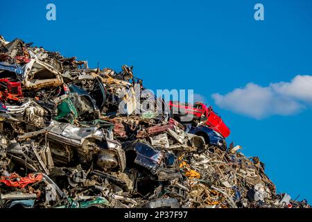 Amidst a messy heap of rusty and crumpled car parts on a junkyard, a red car sits compressed atop other scrapped vehicles. Stock Photo