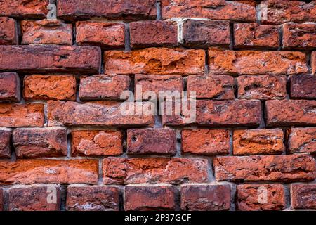 Close-up of a weathered brick wall displays a interplay of varying shades of red, ranging from rusty orange to purple. Stock Photo