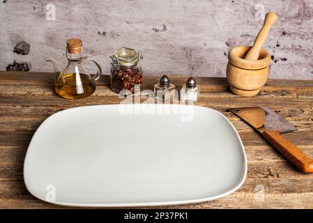 White empty rectangular plate next to salt, pepper, oil and a mortar on an old wooden table. Stock Photo