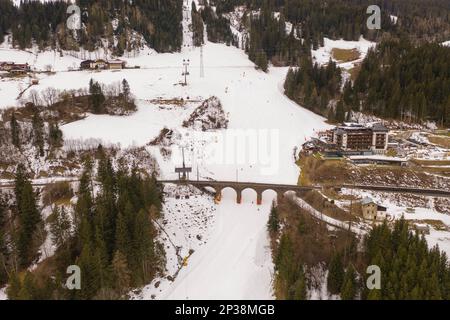 Drone photography of mountain sky slope, railway bridge going over slope and sky lifts during cloudy winter day Stock Photo