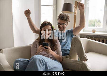 Excited surprised successful young couple using mobile phone together Stock Photo