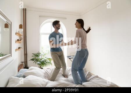 Excited active young couple holding hands, jumping on bed Stock Photo