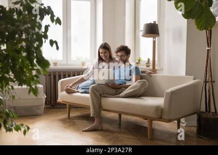 Cheerful millennial young husband and wife using laptop for communication Stock Photo