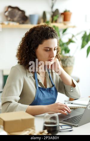 Potter entrepreneur using laptop in workshop, smiling Stock Photo