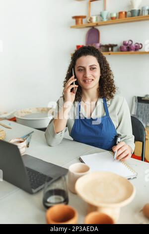 Potter entrepreneur using laptop in workshop, smiling Stock Photo