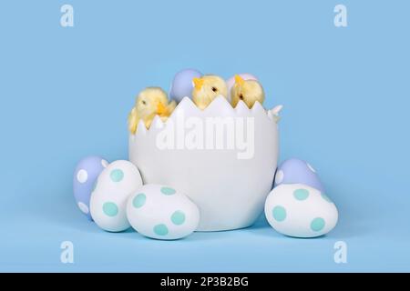 Decorative chicken in large egg shell with painted Easter eggs in front of blue background Stock Photo